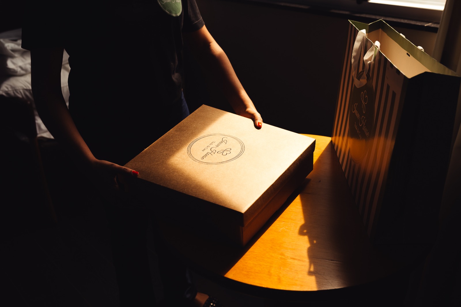 Caixa kraft Inove House sendo entregue, com sacola listrada ao lado em ambiente iluminado pela luz natural